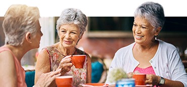 Three elderly women holding mugs and chatting