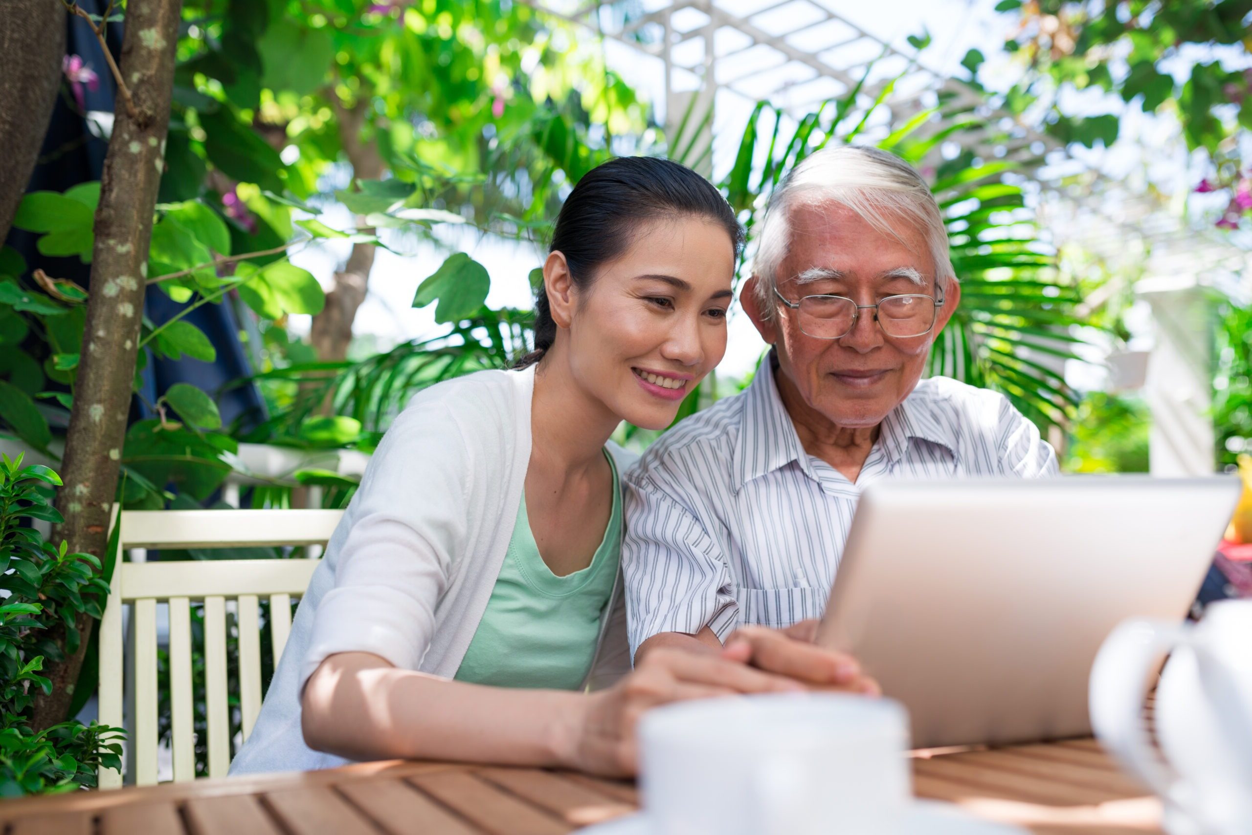 Cheerful Vietnamese father and daughter sitting in outdoor cafe and watching something on tablet computer