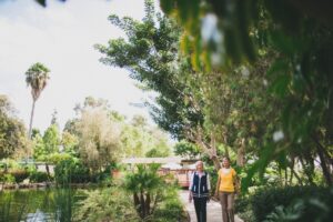 Two women walking together on a paved path in a lush nature area with a pond