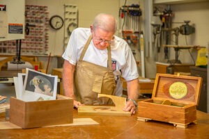 Man in apron at woodworking table focusing on his project
